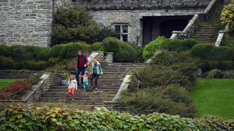 Family of four walking down the steps at the front of Sizergh Castle into the garden. The trees and leaves are red and orange.